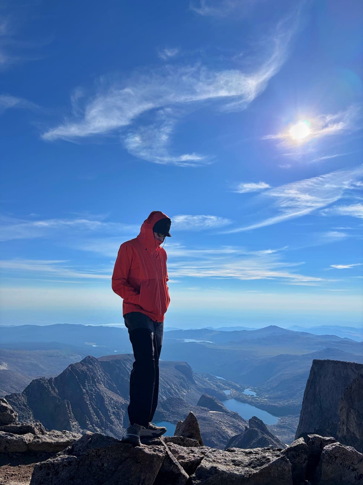 Owen in a red rain jacket on the rocky summit of Cloud Peak, with lakes in the valley far below