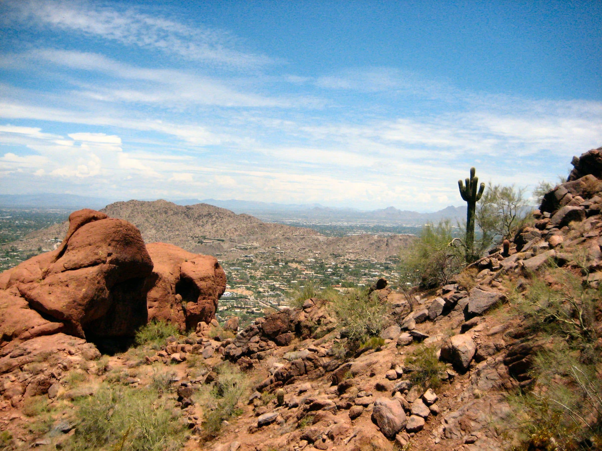 Red sandstone boulders and a lone saguaro on Camelback's rocky slope, with Phoenix spread out below