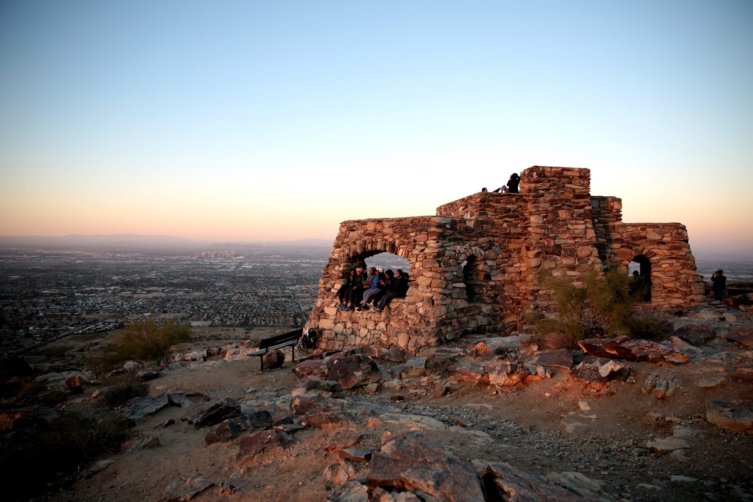 The stone Dobbins Lookout shelter on South Mountain at dusk, with the lights of Phoenix behind it