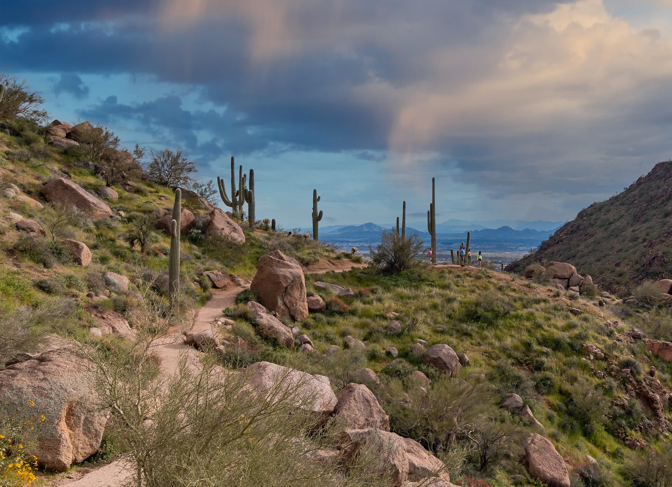 The Pinnacle Peak Trail winding past granite boulders and saguaros under storm clouds