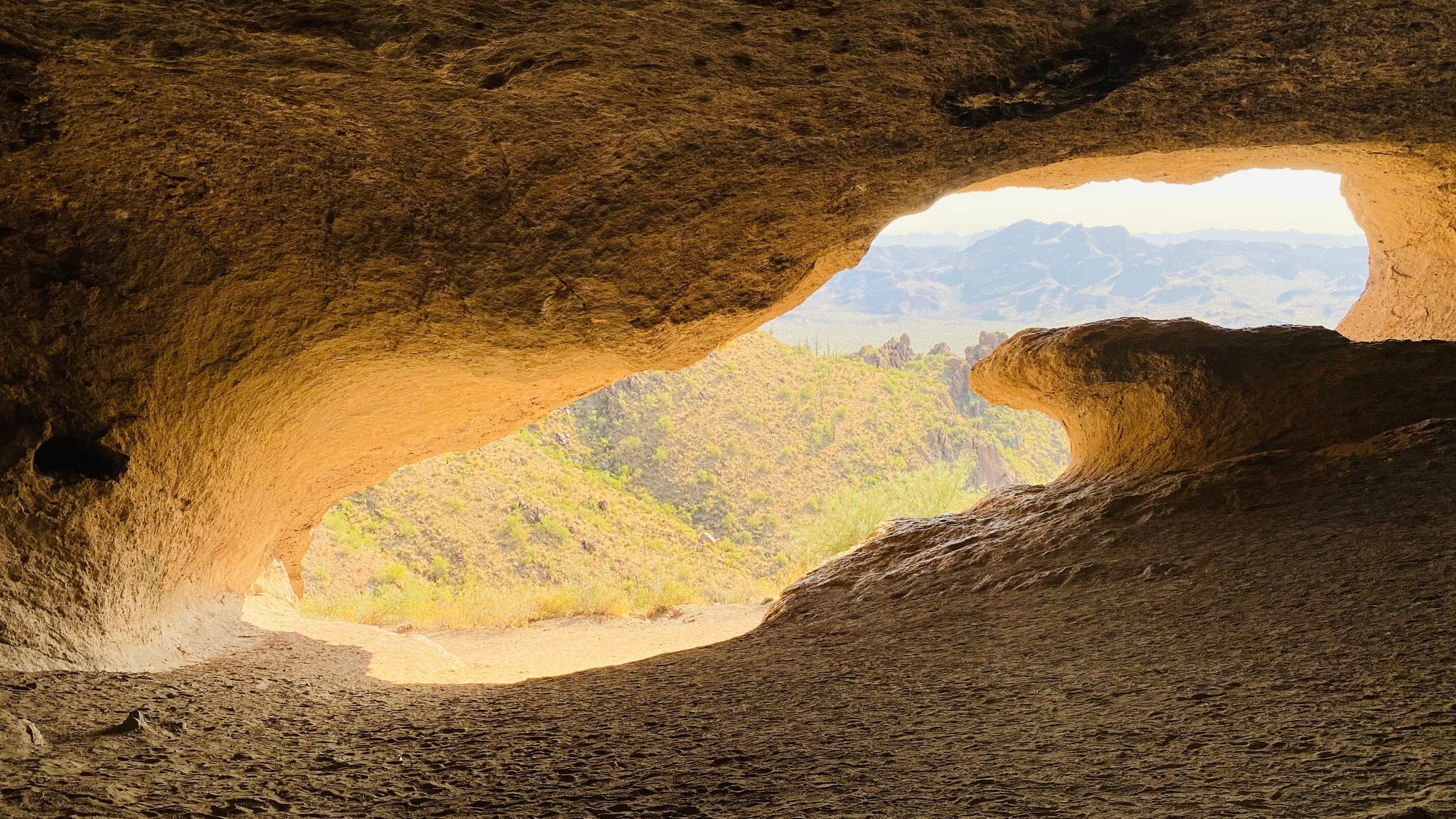 The curling rock lip of Wave Cave framing the desert slopes and mountains beyond